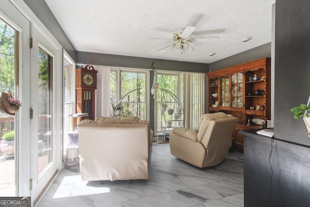 living area featuring plenty of natural light, a textured ceiling, marble finish floor, and ceiling fan