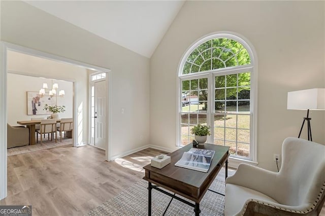 sitting room with high vaulted ceiling, an inviting chandelier, light wood-type flooring, and plenty of natural light