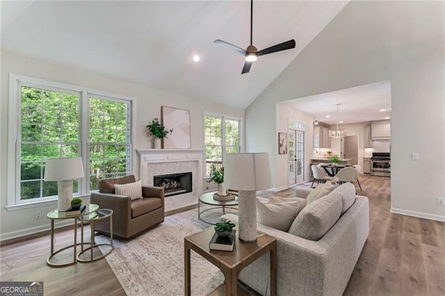 living area with high vaulted ceiling, a ceiling fan, wood finished floors, a fireplace, and baseboards