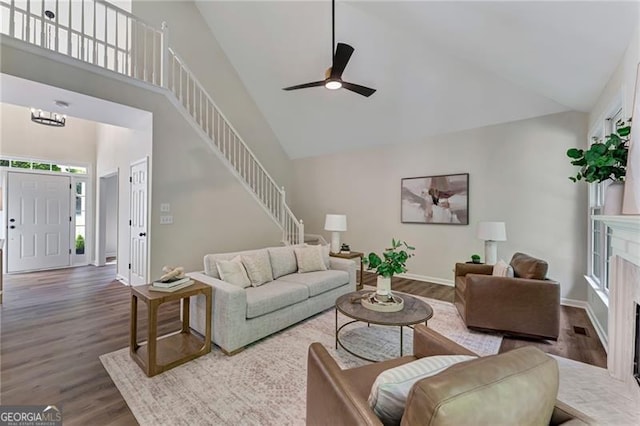 living room featuring baseboards, wood finished floors, stairs, ceiling fan, and high vaulted ceiling