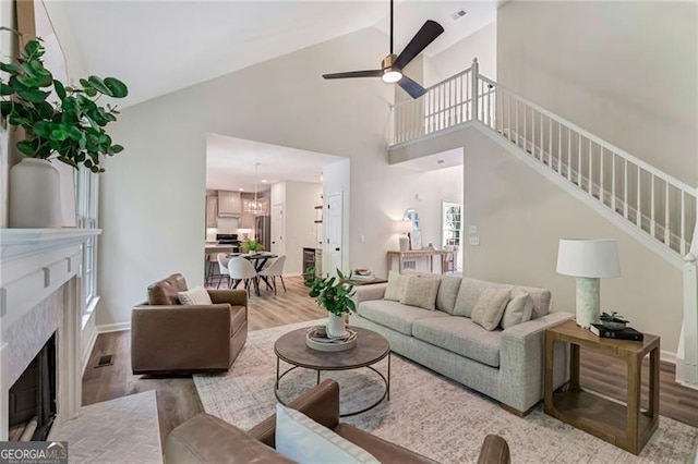 living area featuring stairway, high vaulted ceiling, a ceiling fan, a high end fireplace, and light wood-type flooring