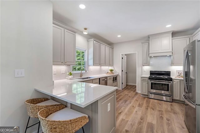 kitchen featuring light wood finished floors, stainless steel appliances, light countertops, a sink, and a peninsula