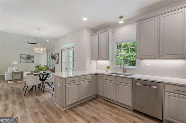 kitchen featuring a peninsula, stainless steel dishwasher, a sink, light wood-style floors, and light countertops