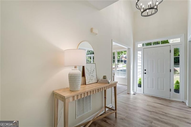 foyer entrance with a wealth of natural light, a notable chandelier, wood finished floors, and a towering ceiling