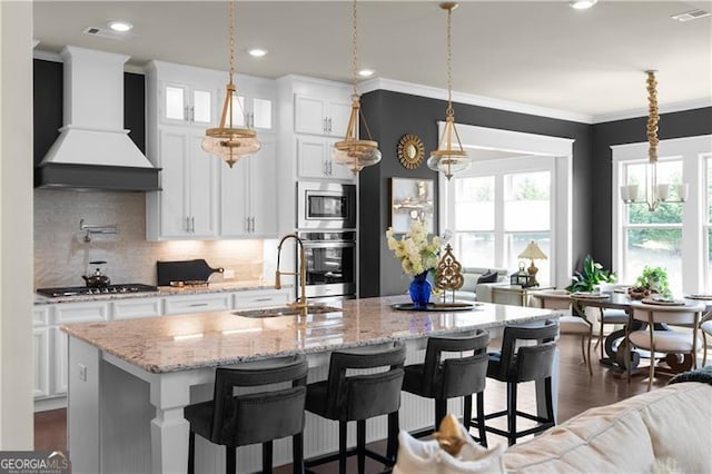kitchen with wall chimney exhaust hood, stainless steel appliances, a sink, open floor plan, and visible vents