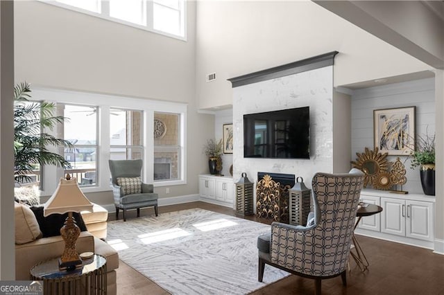 living room with visible vents, baseboards, a towering ceiling, a fireplace, and dark wood-type flooring