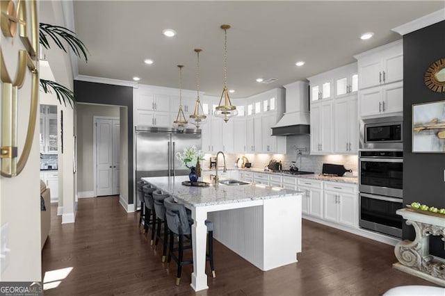 kitchen with white cabinets, built in appliances, a sink, and custom range hood