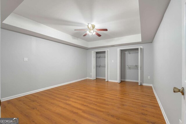 500 Meadowmeade Ln, Lawrenceville, GA 30043 - unfurnished bedroom featuring a raised ceiling, multiple closets, wood finished floors, and ceiling fan