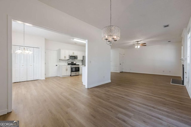 unfurnished living room featuring ceiling fan with notable chandelier, baseboards, light wood finished floors, and visible vents