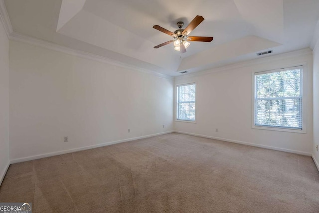 empty room with carpet, a raised ceiling, visible vents, a ceiling fan, and crown molding