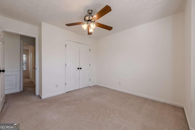 unfurnished bedroom with baseboards, a textured ceiling, a closet, and light colored carpet