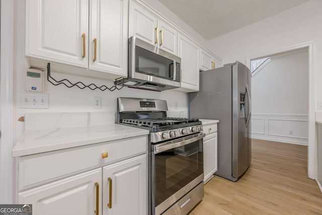 kitchen featuring light stone counters, appliances with stainless steel finishes, light wood-style floors, and white cabinetry