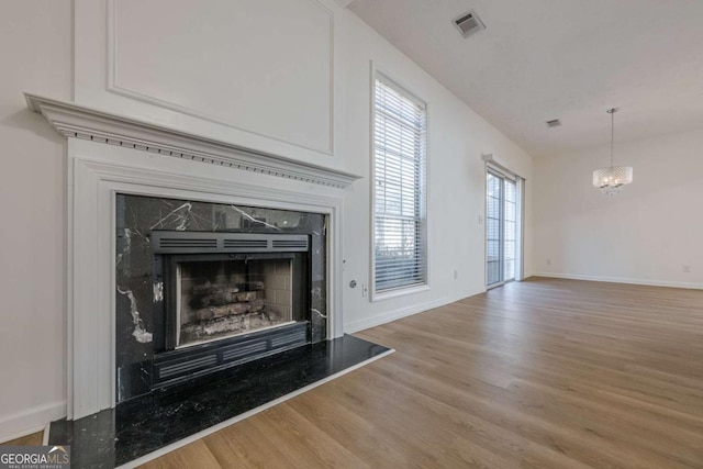 unfurnished living room with an inviting chandelier, wood finished floors, visible vents, a premium fireplace, and baseboards