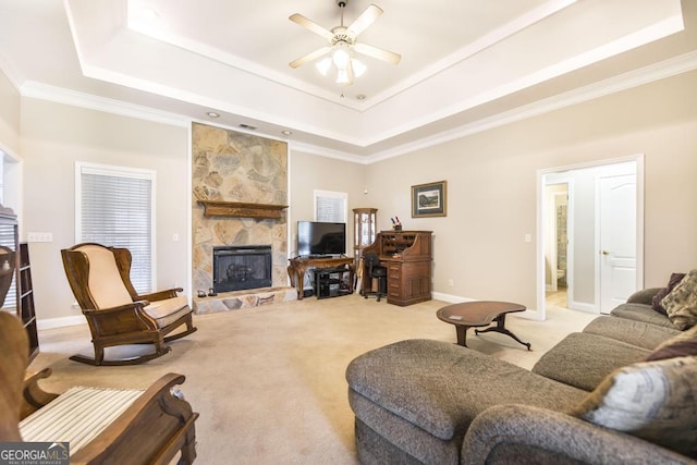 living area featuring light carpet, a stone fireplace, a tray ceiling, and a ceiling fan