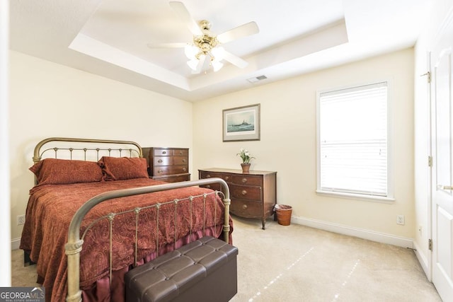 carpeted bedroom featuring a tray ceiling, visible vents, baseboards, and ceiling fan