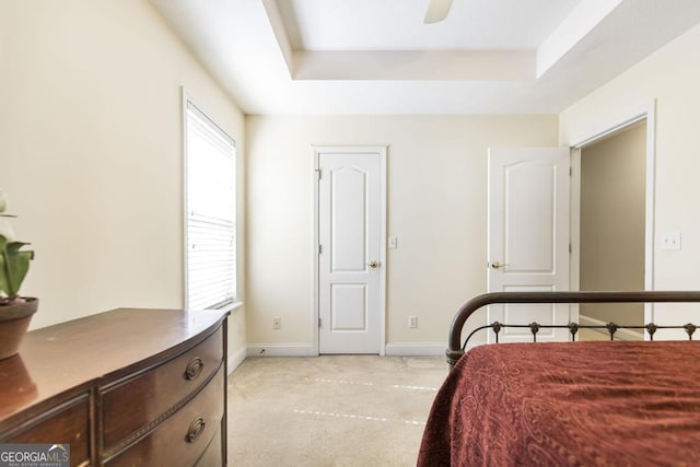 bedroom with baseboards, a raised ceiling, and light colored carpet