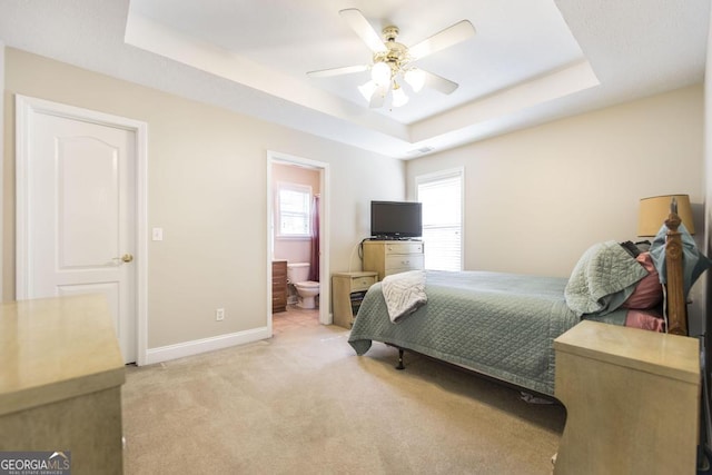 bedroom with ensuite bathroom, ceiling fan, light carpet, a raised ceiling, and baseboards