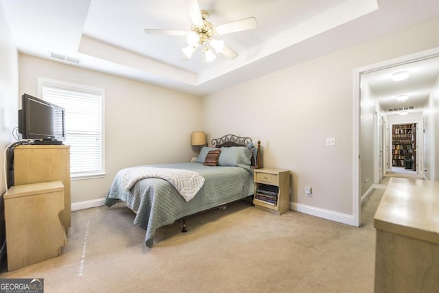 bedroom featuring light colored carpet, baseboards, a tray ceiling, and visible vents