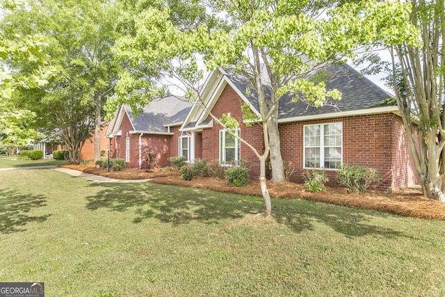 view of front of house with brick siding, roof with shingles, and a front yard