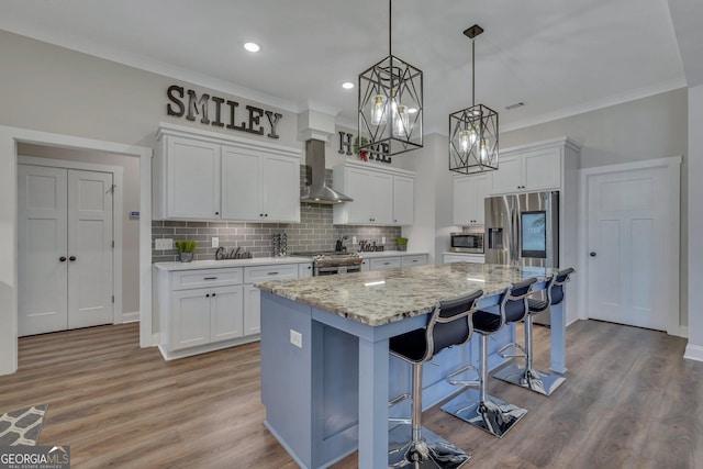 kitchen with wall chimney exhaust hood, stainless steel appliances, white cabinets, backsplash, and a kitchen island