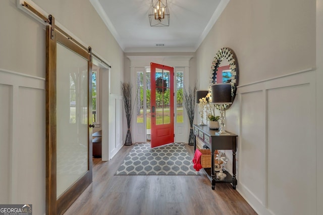 entrance foyer with wood finished floors, a decorative wall, ornamental molding, and a barn door
