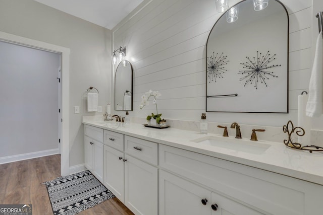 full bathroom featuring double vanity, wood finished floors, baseboards, and a sink