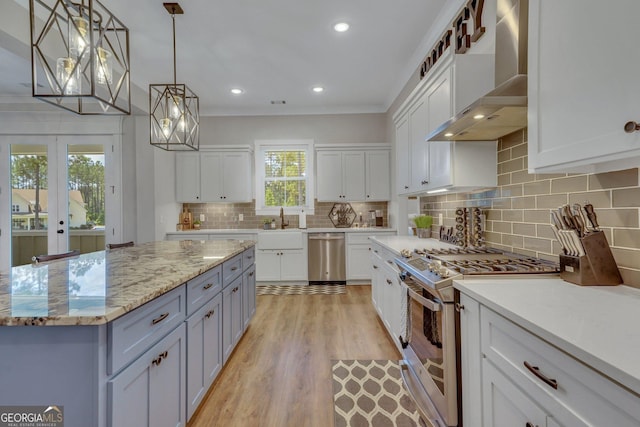 kitchen featuring stainless steel dishwasher, a sink, wall chimney exhaust hood, gas range, and white cabinetry