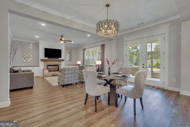 dining area featuring ceiling fan with notable chandelier, french doors, light wood finished floors, a fireplace, and ornamental molding