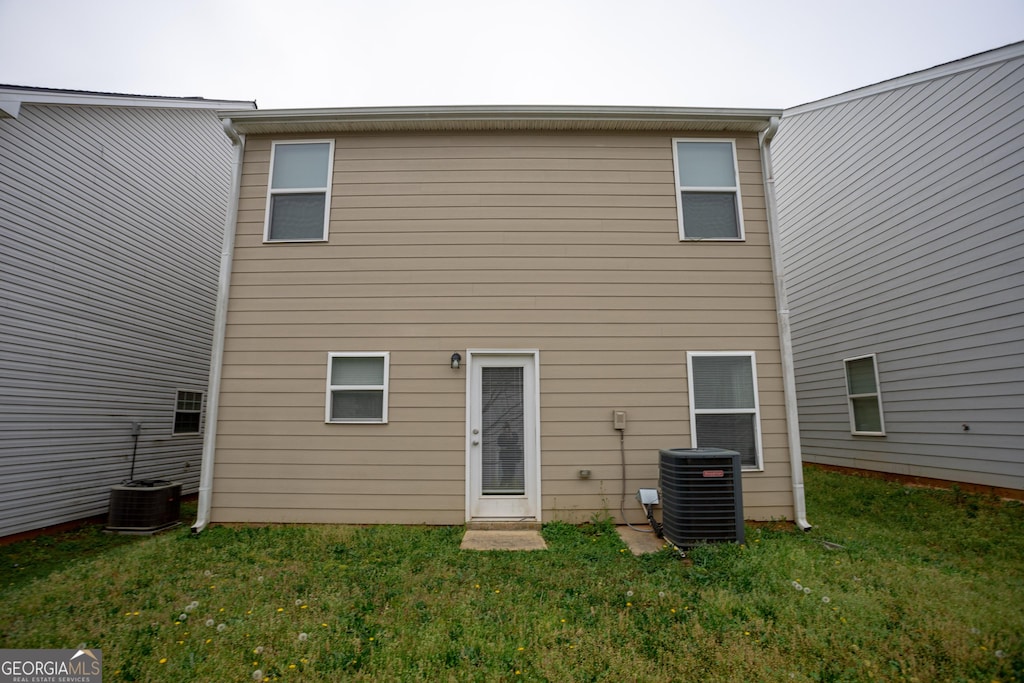 rear view of property with central air condition unit and a yard