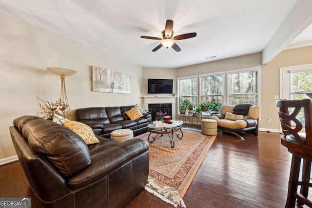 living room featuring dark wood finished floors, baseboards, visible vents, a premium fireplace, and a ceiling fan