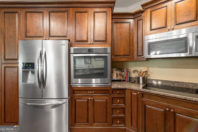 kitchen featuring brown cabinets, appliances with stainless steel finishes, and dark stone countertops