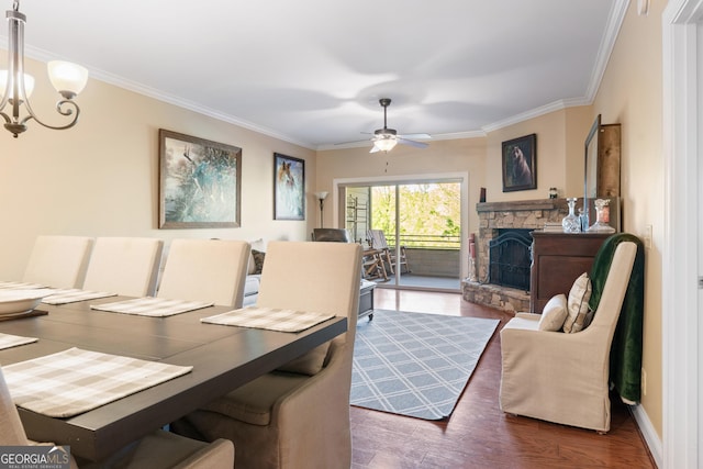 dining space with a stone fireplace, ornamental molding, wood finished floors, and ceiling fan with notable chandelier