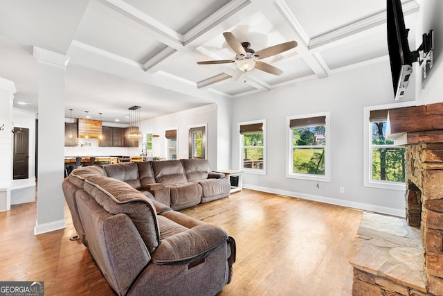 living area featuring light wood finished floors, beamed ceiling, a ceiling fan, a stone fireplace, and ornamental molding