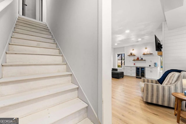 stairs featuring wood finished floors, beverage cooler, a bar, and recessed lighting