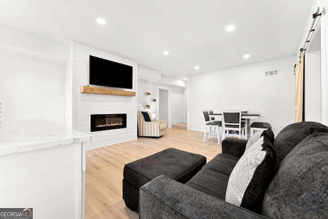 living area featuring a barn door, recessed lighting, visible vents, light wood-style flooring, and a large fireplace