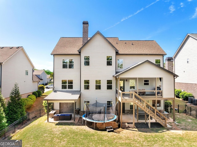 rear view of house with stairway, a trampoline, a chimney, a fenced backyard, and a yard