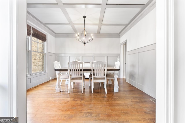 dining space with a decorative wall, light wood-style floors, coffered ceiling, a notable chandelier, and beam ceiling