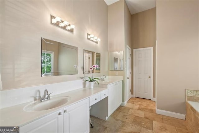 full bath featuring double vanity, a bath, baseboards, and a towering ceiling