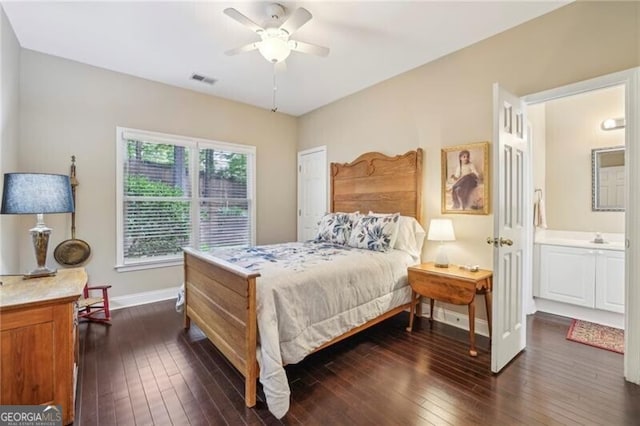 bedroom featuring baseboards, dark wood-type flooring, ensuite bathroom, a sink, and a ceiling fan