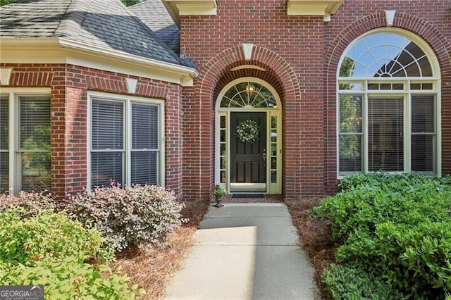 property entrance featuring brick siding and roof with shingles