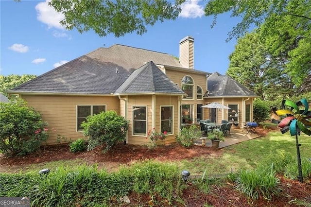 back of house featuring a chimney, a patio area, a yard, and roof with shingles