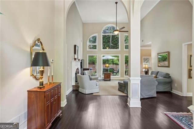 living area featuring arched walkways, a high ceiling, a ceiling fan, dark wood-style flooring, and baseboards