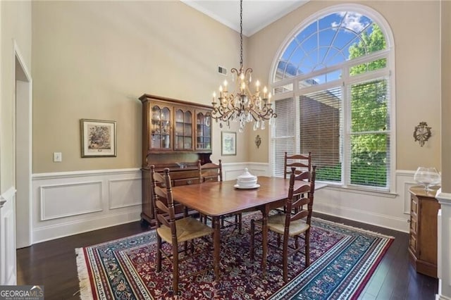 dining room with a chandelier, dark wood-style flooring, wainscoting, a decorative wall, and ornamental molding