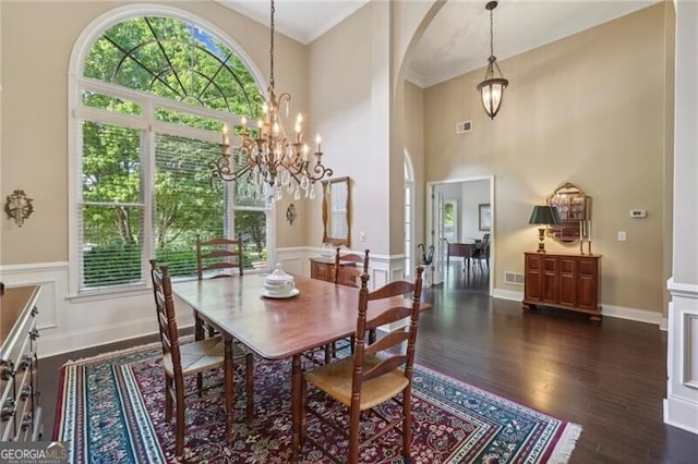 dining room featuring arched walkways, healthy amount of natural light, a chandelier, dark wood-type flooring, and a high ceiling