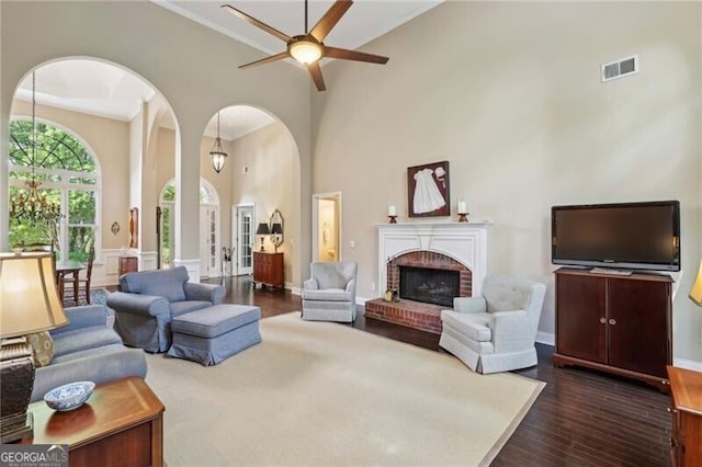 living area with arched walkways, ceiling fan, dark wood-style flooring, a brick fireplace, and a high ceiling