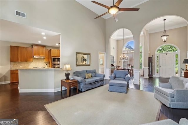 living area with arched walkways, dark wood-style flooring, a high ceiling, crown molding, and a chandelier