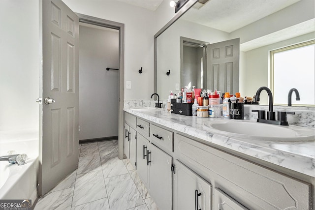bathroom with double vanity, marble finish floor, a tub, and a sink