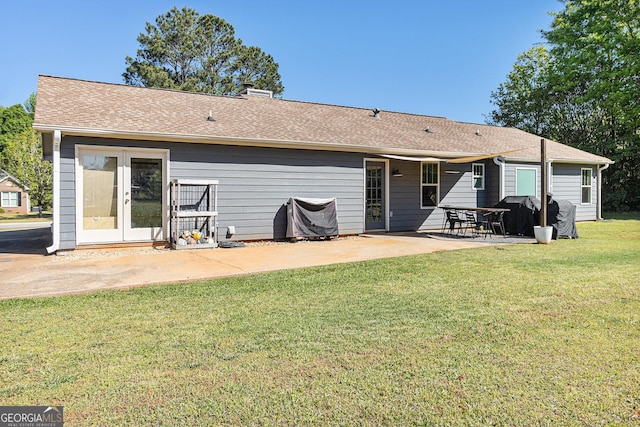 back of house featuring a lawn, roof with shingles, and a patio area