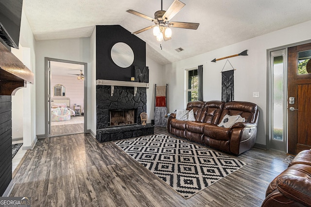 living area featuring plenty of natural light, wood finished floors, a stone fireplace, and ceiling fan