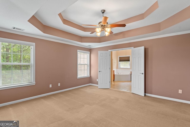 unfurnished bedroom featuring visible vents, a raised ceiling, light colored carpet, and multiple windows